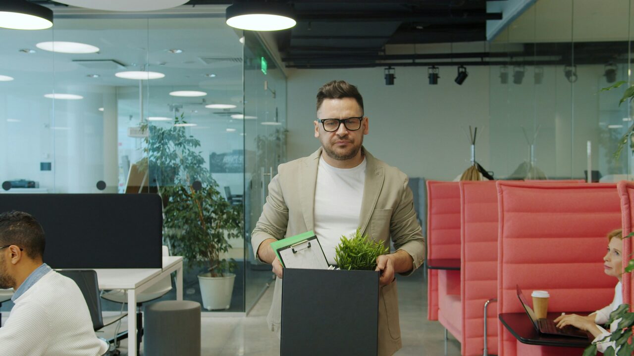 Terminated employee carrying a box of personal belongings out of an office